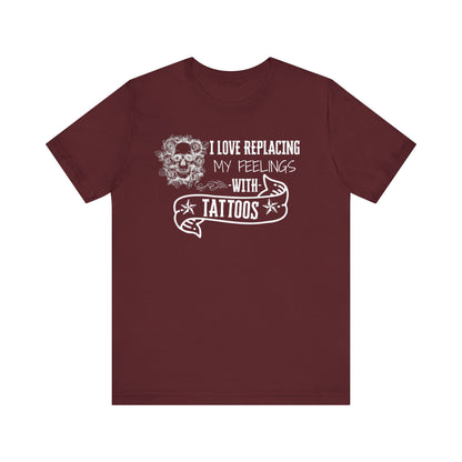 A sarcastic graphic tee stating 'I love replacing my feelings with tattoos' in color maroon