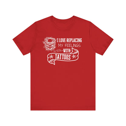 A sarcastic graphic tee stating 'I love replacing my feelings with tattoos' in color red