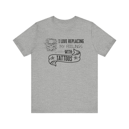 A sarcastic graphic tee stating 'I love replacing my feelings with tattoos' in color athletic heather