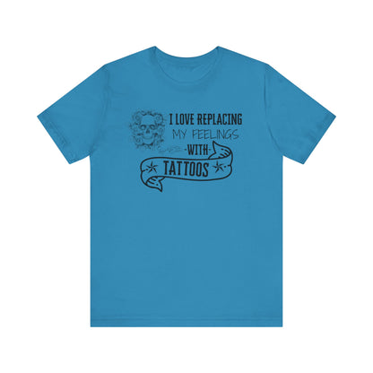 A sarcastic graphic tee stating 'I love replacing my feelings with tattoos' in color aqua