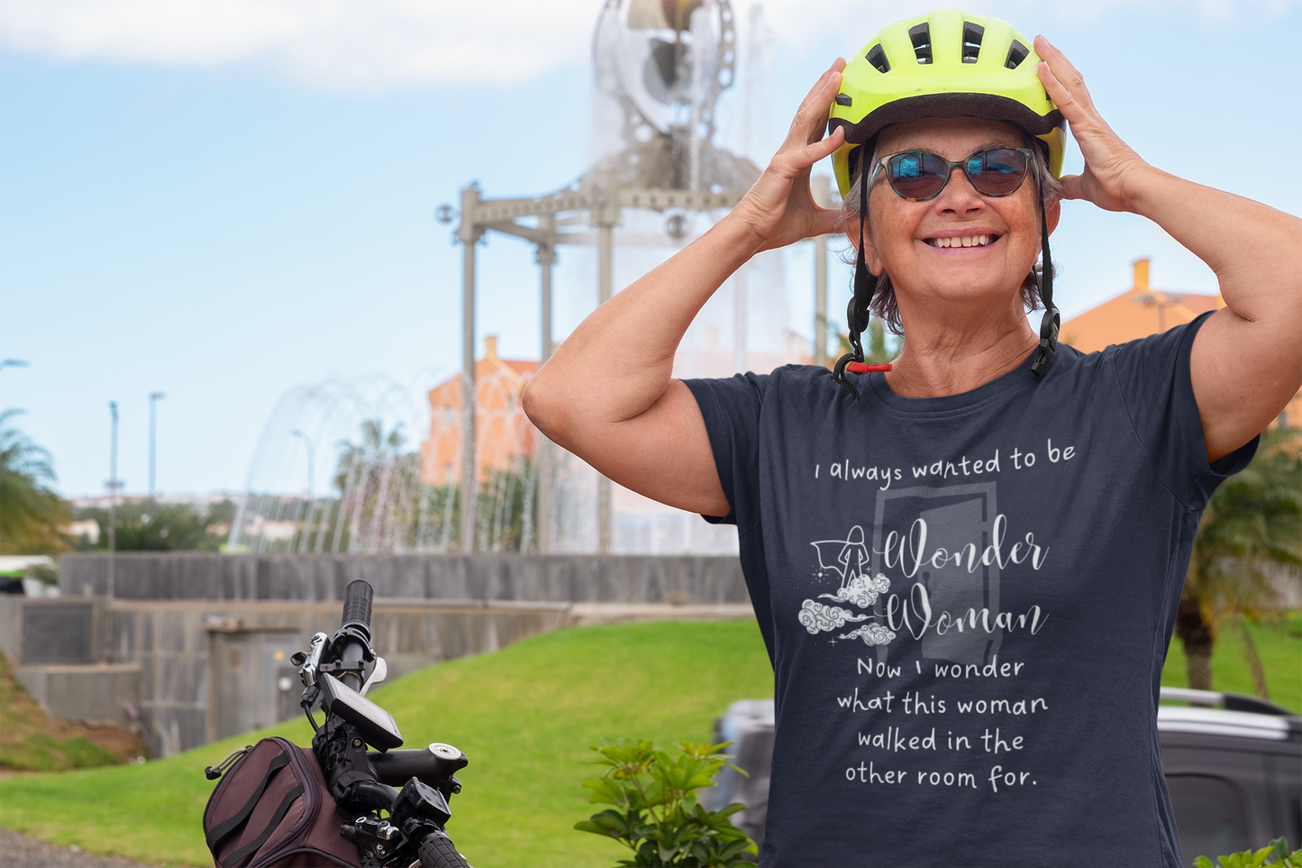 Woman with grey hair and a bike helmet wearing sunglasses and a shirt stating I always wanted to be Wonder Woman. Now I wonder what this woman walked in the other room for. In color Navy.