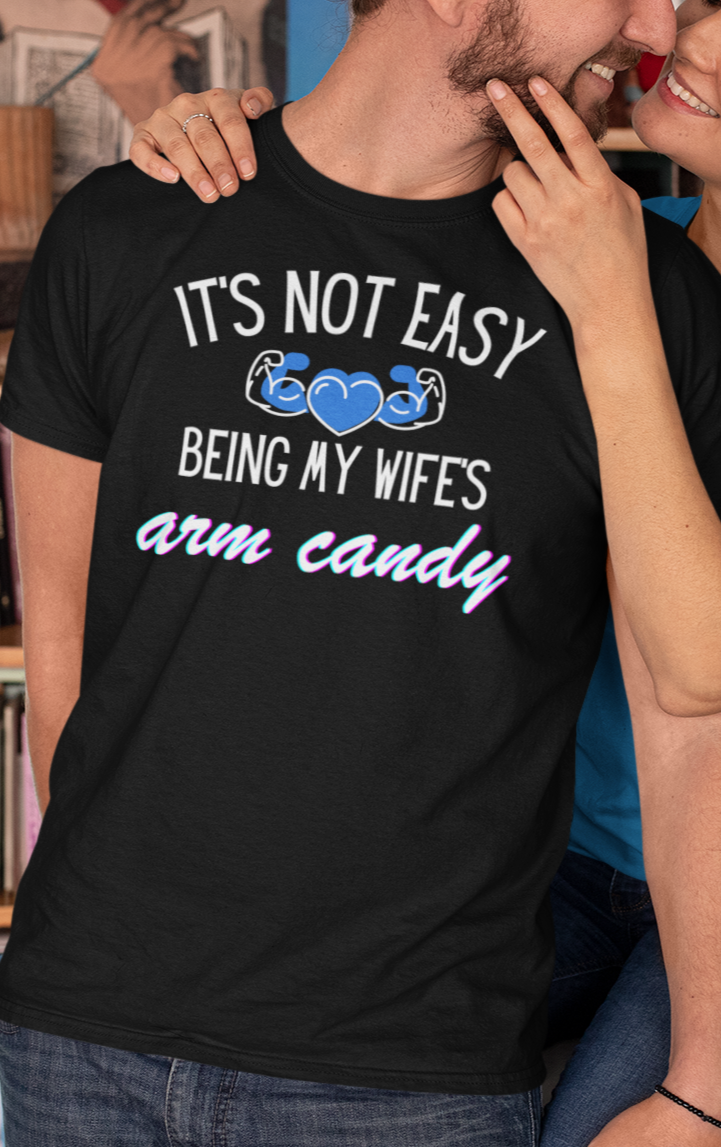 Man smiling with wife wearing a graphic tee stating It's Not Easy Being My Wife's Arm Candy in color black