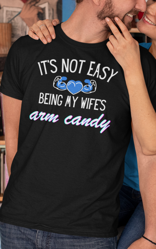 Man smiling with wife wearing a graphic tee stating It's Not Easy Being My Wife's Arm Candy in color black